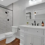 bathroom with gray tiled shower, white toilet, and a sleek vanity
