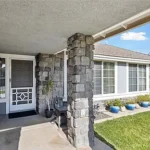 Front porch of a house with a stone pillar, gray door, and a row of blue potted plants