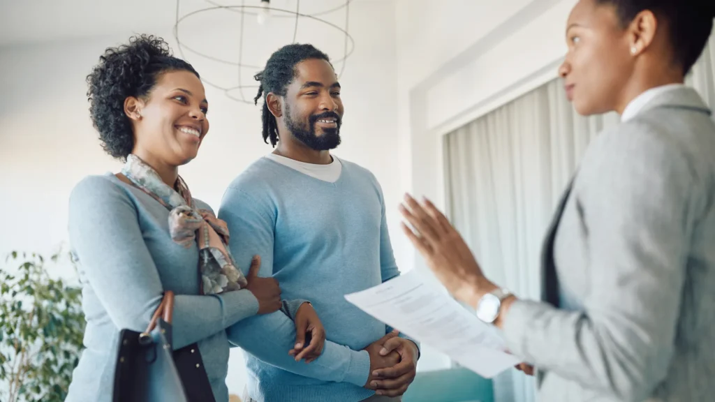 A smiling couple talks to a realtor in an office