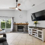 living room with a gray couch, stone fireplace, and wall-mounted TV