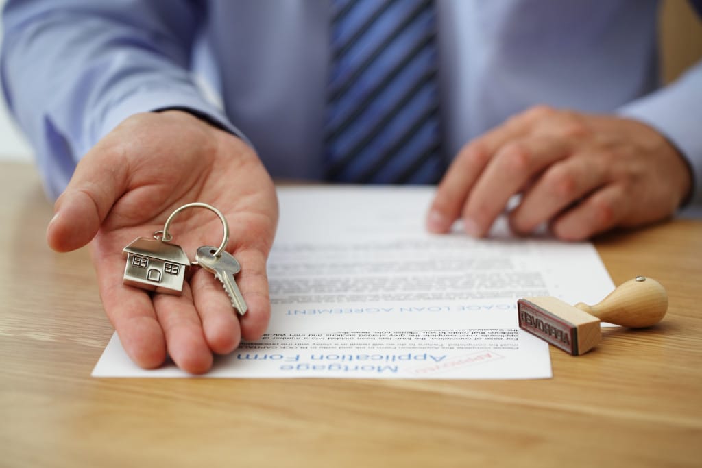 A hand extends a house-shaped keychain and a key over a mortgage application form